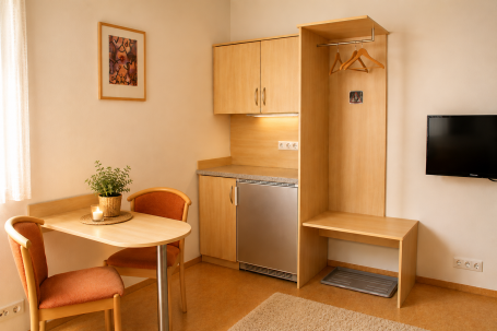 Zimmer 8 Kleine Wohnung mit einem Esstisch, Kühlschrank und Garderobe.