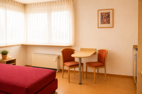 Zimmer 8 Helle Zimmeransicht mit einem Tisch, zwei Stühlen und einem roten Sofa.