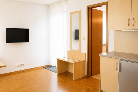 Zimmer 7 Helle, moderne Wohnung mit Fernseher, Tisch und Sicht auf die Tür.