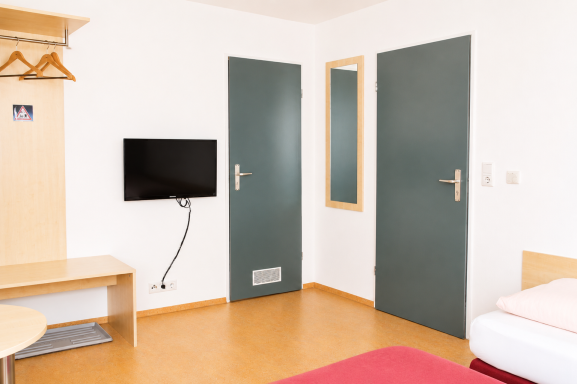 Zimmereinrichtung Helle Hotelzimmer mit einem Bett, Fernseher, Tisch und zwei Türen.