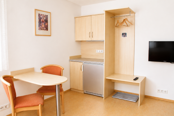 Zimmereinrichtung Kleine Wohnung mit Tisch, Stühlen, Küchenzeile und TV in neutralem Design.