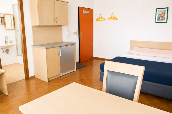 Zimmereinrichtung Heller Hotelzimmer mit einem Bett, Tisch, Kühlschrank und Badezimmerbereich.