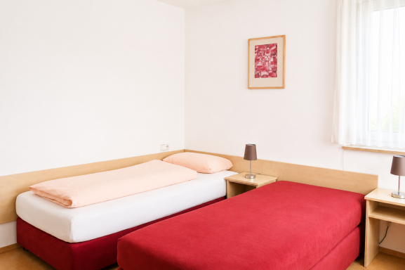 Zimmereinrichtung Helles Zimmer mit einem Einzel- und einem Doppelbett sowie Nachttischen.