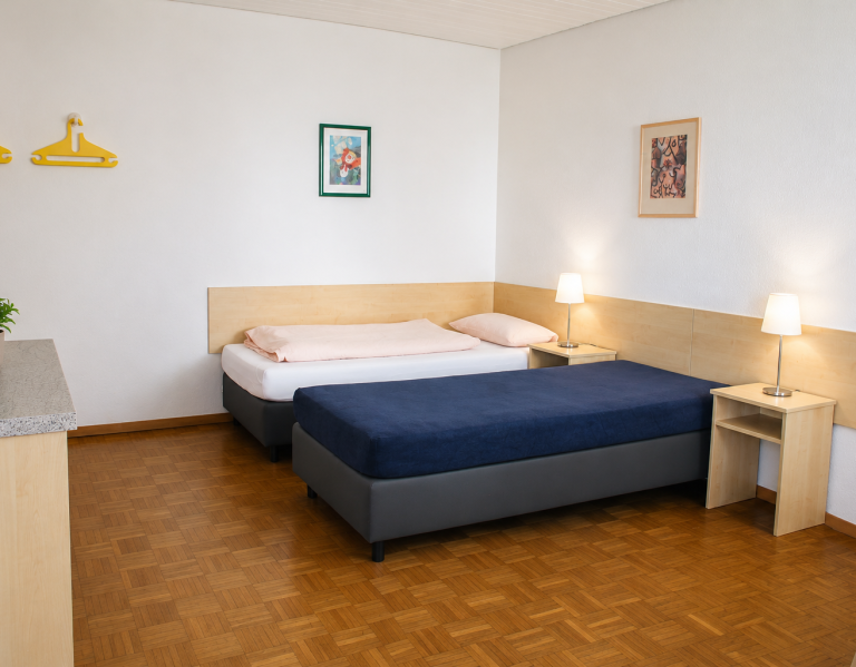 Betten Gästezimmer Helles Hotelzimmer mit zwei Betten, Nachttisch und einempflanzen.