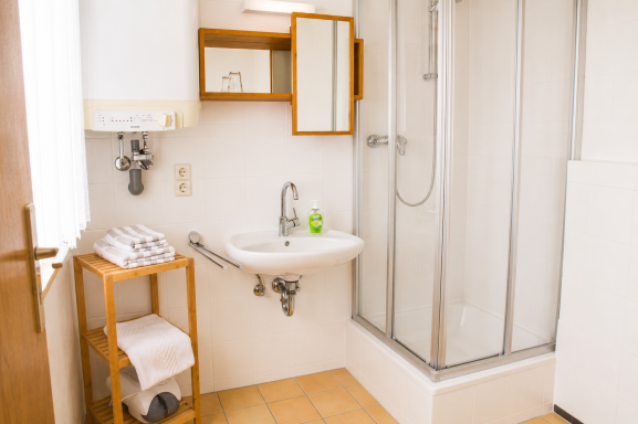 Badezimmer Helles Badezimmer mit Dusche, Waschbecken und Holzregal.